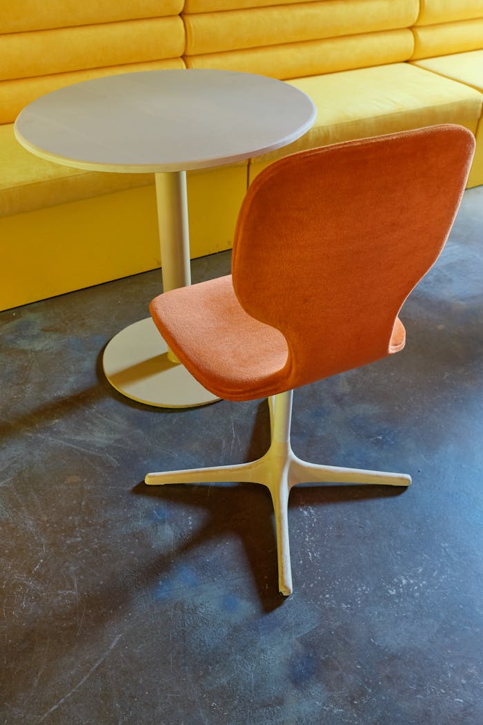 Mastering the First Impression: Your intriguing post title goes here Contemporary orange chair with round table against yellow bench, showcasing modern interior décor.